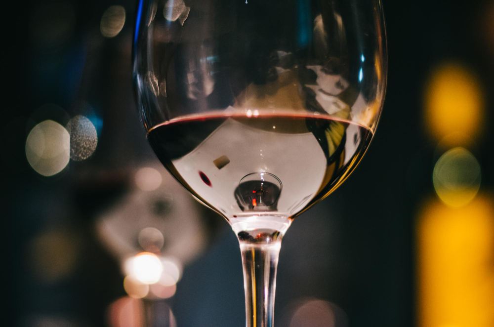 gros plan sur un verre à vin transparent contenant un peu de vin rouge, avec des reflets flous lumineux en arrière-plan